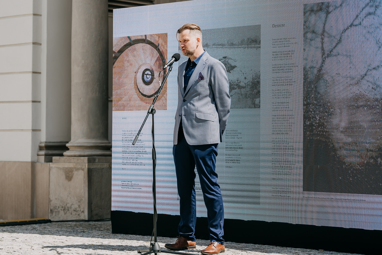 Mężczyzna przemawiający na tle dużej ekspozycji multimedialnej